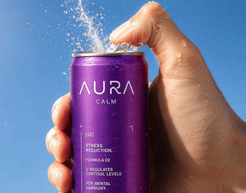 A hand opening a purple AURA Calm can against a blue sky