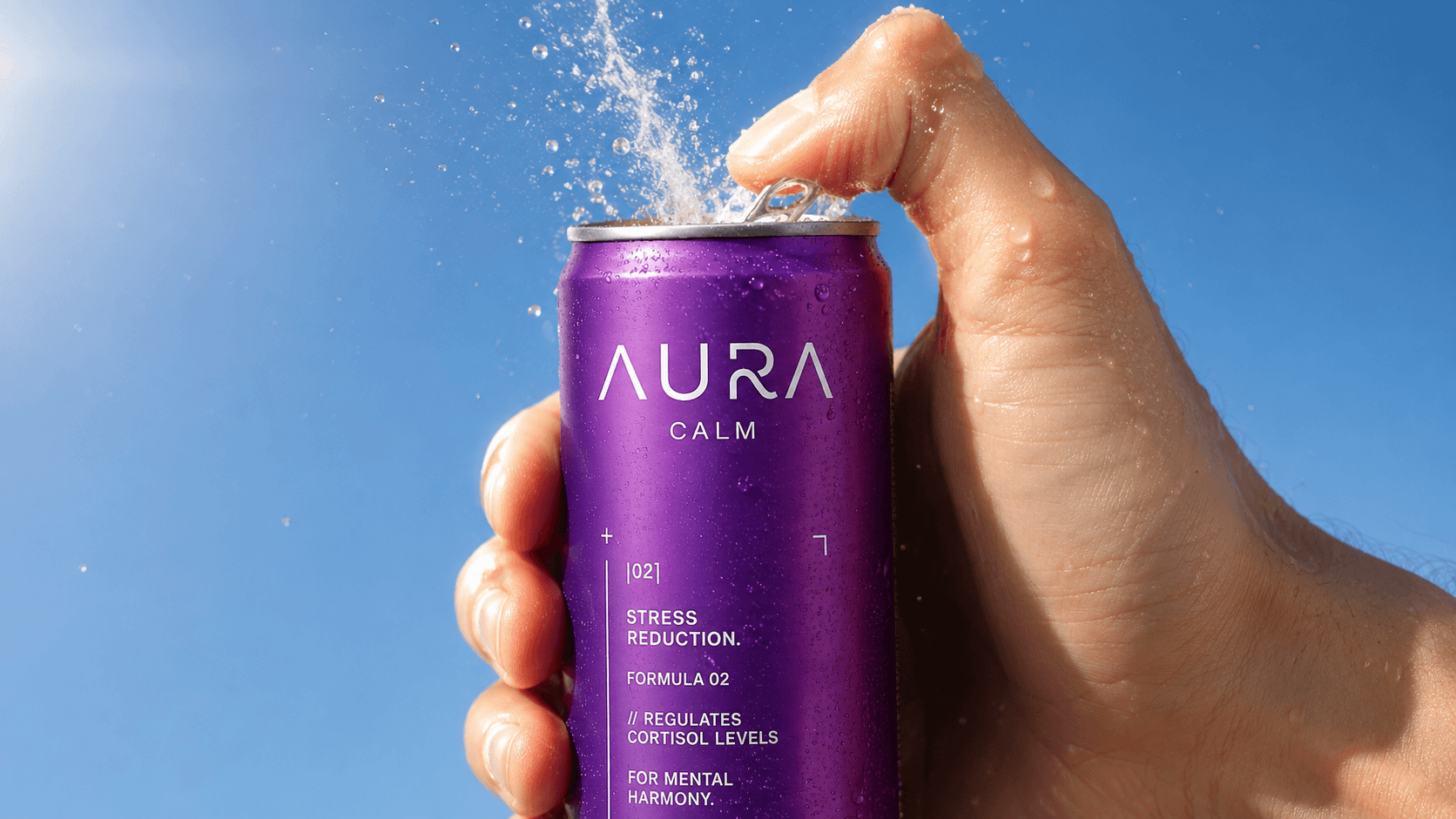 A hand opening a purple AURA Calm can against a blue sky.