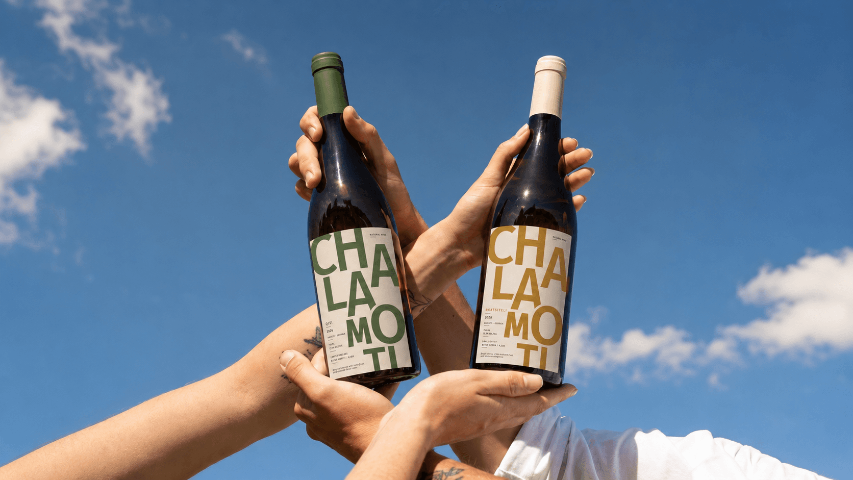 Two CHALAMOTI wine bottles raised against a blue sky.