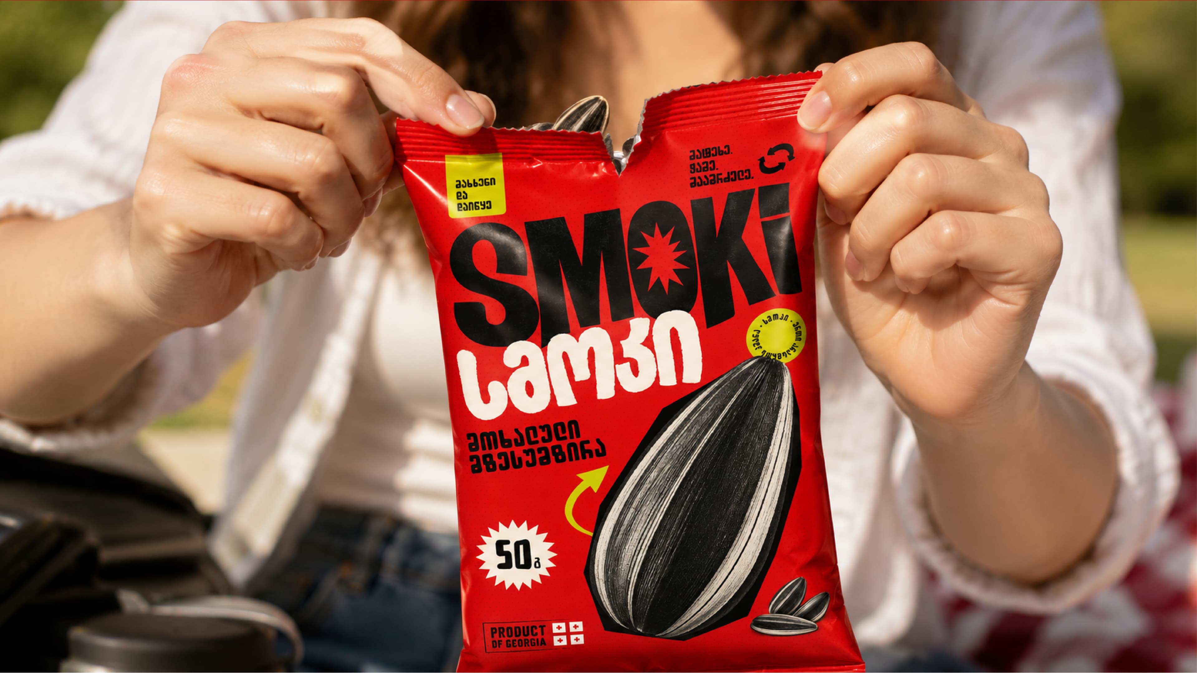 Hands opening the red SMOKI sunflower seed package.