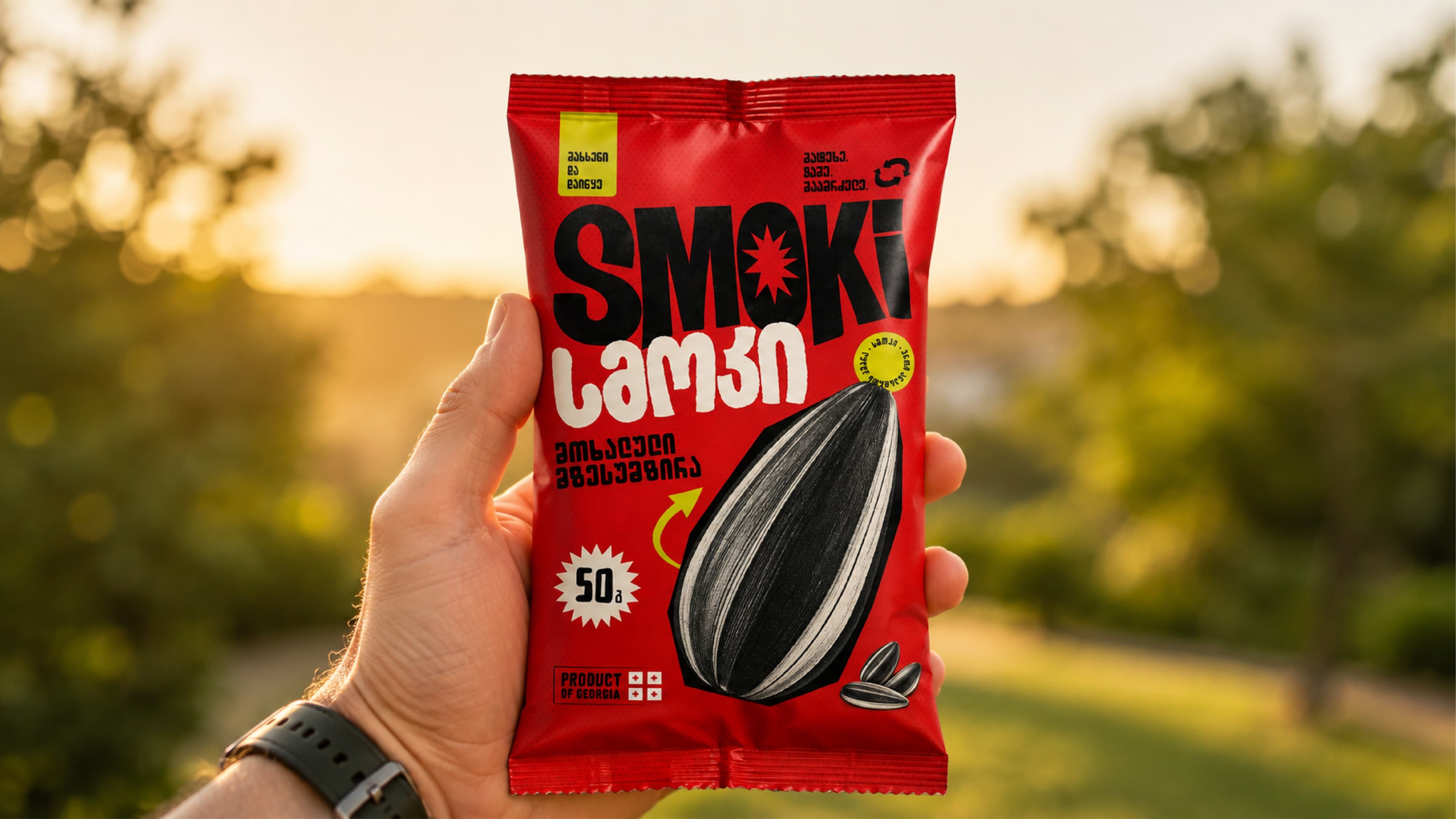 A hand holding the redesigned red SMOKI package outdoors in warm evening light.